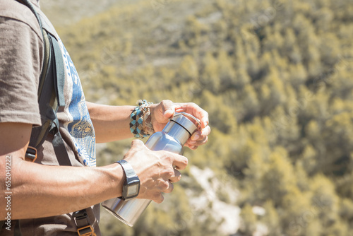 Hand taking an aluminum thermal bottle to hydrate on a hiking trail