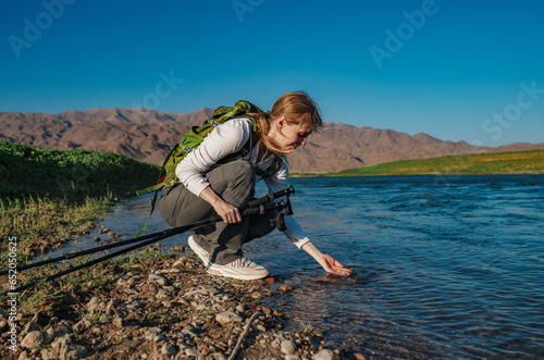 Young woman tourist touching water in mountain river with her hand