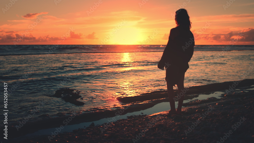 Woman silhouette against amazing colorful sunset sky over ocean waves. Slim girl stand on coast beach relax and enjoy wild nature beauty on tropical island. Travel, tourism, holiday, active lifestyle