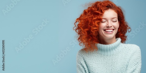 Portrait of a young red haired woman with pleasant smile over pastel background, bannerwith copy space. Beautiful girl in warm sweater photo