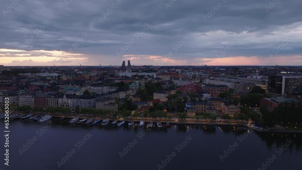 Sliding reveal of waterfront in evening city. Aerial view of boats at bank and buildings in urban borough. Silhouette of Norra Tornen high rise towers in background. Stockholm, Sweden Sliding reveal of waterfront in evening city. Aerial view of boats at bank and buildings in urban borough. Silhouette of Norra Tornen high rise towers in background. Stockholm, Sweden
