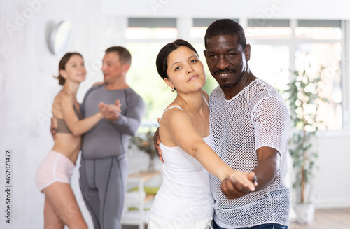 Positive woman and African american man practicing bachata dance moves in pair during group class in dancing studio