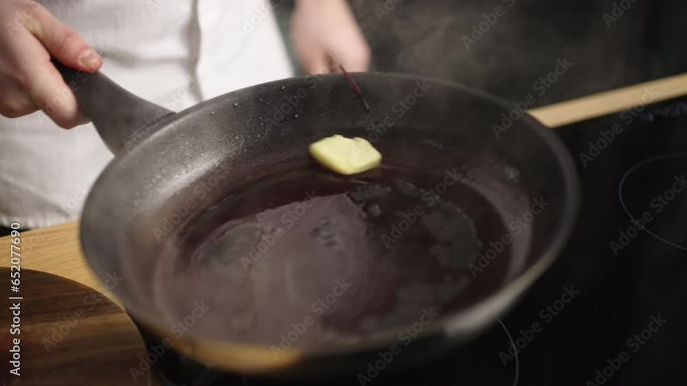 A piece of butter being added to a pan by the chef in the kitchen. Chef making the pan buttery A piece of butter being added to a pan by the chef in the kitchen. Chef making the pan buttery