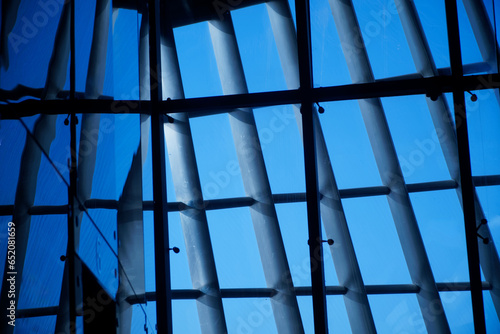 Intersecting metal beams in architecture supporting glass walls. Interior. Blue sky through the glass walls of a modern office space. Photo.