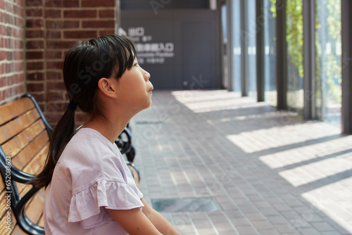 夏の博物館のベンチで休憩している小学生の女の子の様子