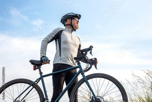 Bearded man cyclist stands with a bike against the blue sky. cycling and health hobbies