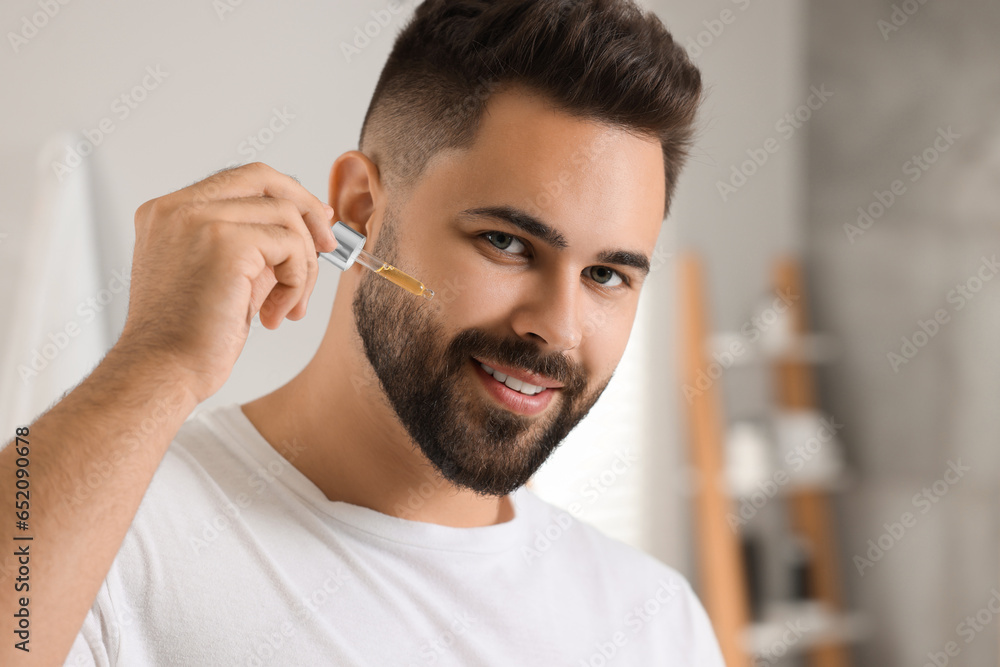 Obraz premium Handsome man applying cosmetic serum onto his face in bathroom