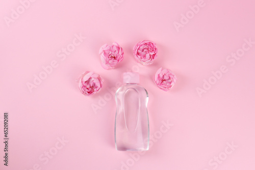 Bottle with baby oil and beautiful flowers on pink background, flat lay. Space for text © New Africa