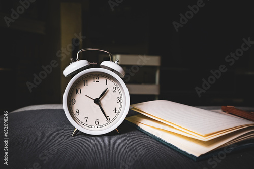 The clock and note book in the dark room background for time management and work concept.
