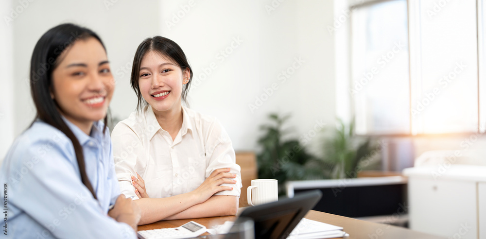 Portrait of young successful woman sitting at co-workspace with her colleague, smiling to camera. Portrait of young successful woman sitting at co-workspace with her colleague, smiling to camera.