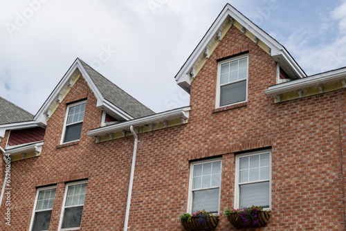 A row of brown brick townhouses with peaked gable roofs, and double hung windows with white trim. The shingles are black asphalt. The adjoined facade row houses are multi story residential buildings. 