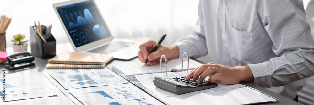 Corporate auditor calculate budget with calculator in office with BI dashboard on laptop screen. Professional accountant of accounting company analyze financial document for profitable income. Insight - obrazy, fototapety, plakaty 