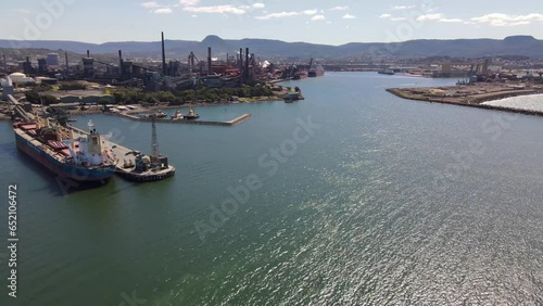 Aerial drone pullback reverse view of Port Kembla, in the Illawarra Region of NSW, Australia showing the seaport, industrial complex and harbour on a sunny day  photo