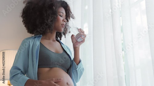 Woman tenderly caressing baby bump while sipping water