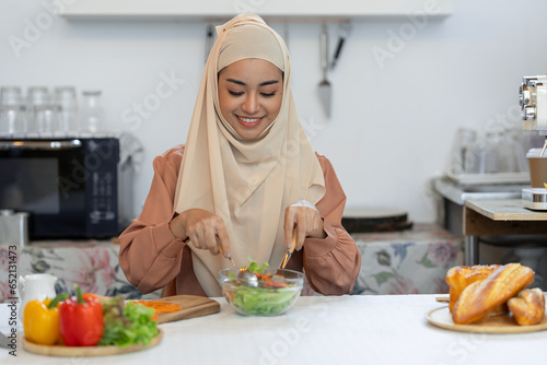 Young Muslim woman in hijab eats vegetable salad healthy food in the kitchen Fasting concept, vegetarian diet, vegan diet