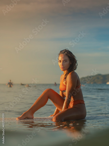 Ethnic woman sitting on a surfboard in the evening
