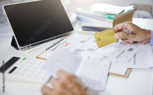 Accountant using tablet work on desk holding credit card and checking savings book, receipt, bank statement and business document calculate expenses paid via credit card before finalizing the account photo