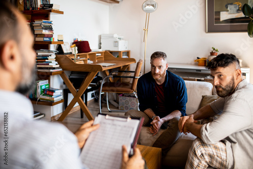 Young male gay caucasian couple talking to their therapist or counselor at home in the living room