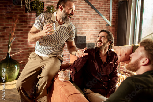 Male friends drinking whiskey and telling stories at home in the living room photo