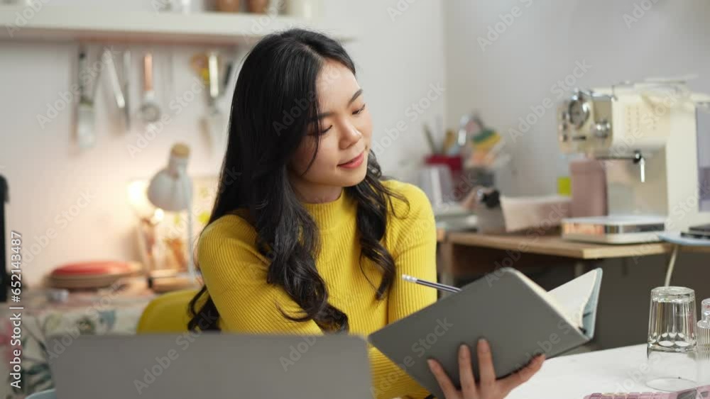 Smiling happy beautiful Asian woman relaxing using technology of laptop computer. take note of information Have a relaxing hot drink while sitting on the table in your room at home. Smiling happy beautiful Asian woman relaxing using technology of laptop computer. take note of information Have a relaxing hot drink while sitting on the table in your room at home.