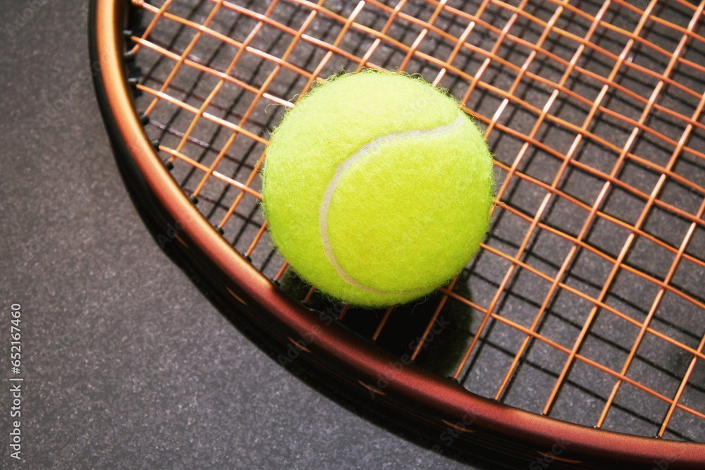 Modern brown tennis racquet with yellow ball on the strings. Isolated on reflective black. Recreational sports backgrounds