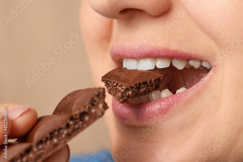 Close up of the mouth of a Caucasian woman biting off a piece of porous chocolate. Three-quarter front view. Low angle view. photo