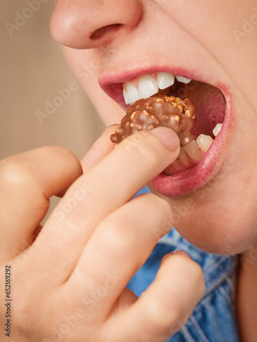 Close up happy Caucasian woman puts a piece of chocolate bar with nuts into her open mouth. Three-quarter front view. Low angle view. Vertical frame.