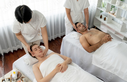 Caucasian couple enjoying relaxing anti-stress head massage and pampering facial beauty skin recreation leisure in dayspa modern light ambient at luxury resort or hotel spa salon. Quiescent