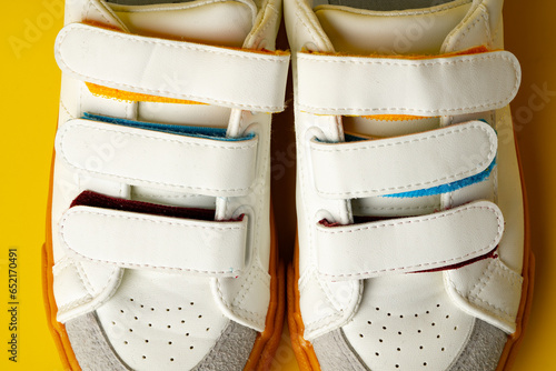 White leather sneakers with fasteners on yellow background