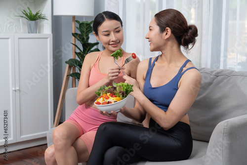 Young sporty Asian women in sportswear holding salad bowl together fill with vibrant of fruit and vegetable. Natural youthful and fit body lifestyle with balance nutrition and home exercise. Vigorous