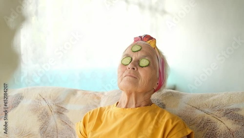 Portrait of an elderly woman with gray hair with cucumber slices on her face. The concept of anti-aging skin care at home.