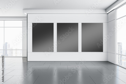 Modern gallery interior with clean black mock up banners on white concrete wall, flooring with reflections and window with city view and daylight. 3D Rendering. © Who is Danny