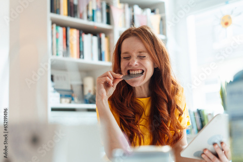 Happy woman biting credit card and holding tablet PC at home photo