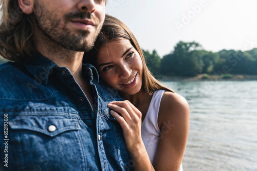 Smiling young woman leaning against man's shoulder at the riverside photo