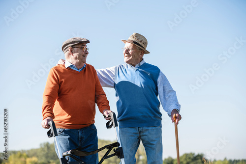 Old friends taking a stroll in the fields with walking stick and wheeled walker, talking about old times photo