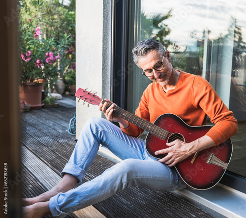 Smiling man playing guitar sitting on porch seen through glass photo