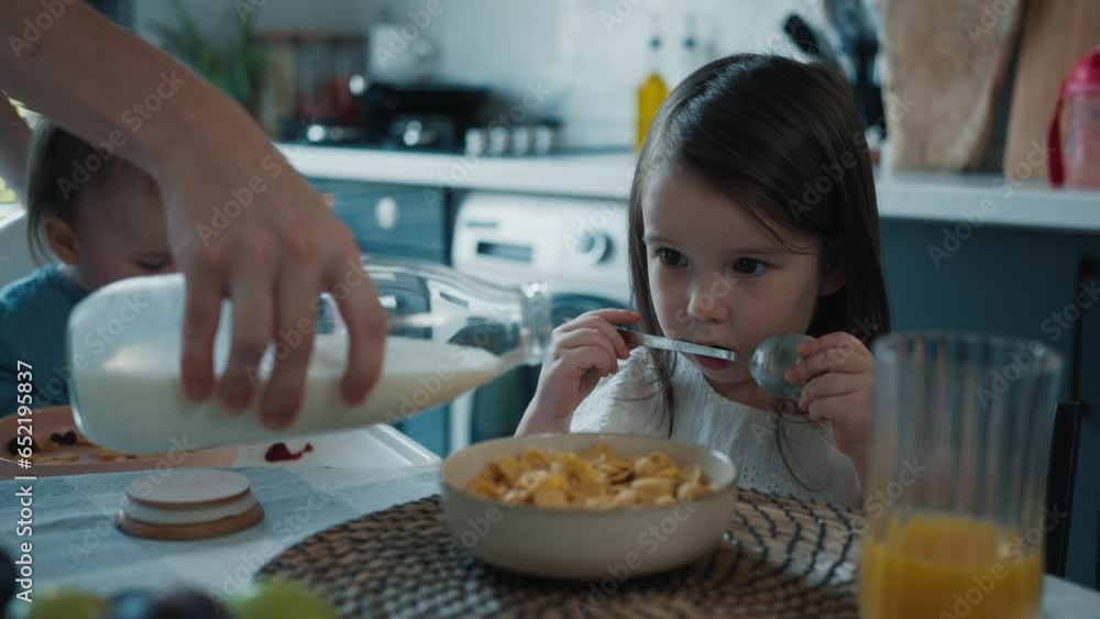 Mother Pours Corn Flakes for Breakfast into her Little Baby Daughter's Bowl Mother Pours Corn Flakes for Breakfast into her Little Baby Daughter's Bowl