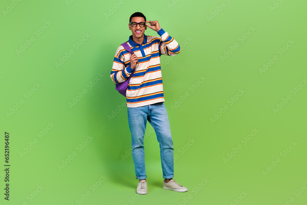 Full body photo of young man smile touch eyeglasses posing model wear rucksack back to cambridge college isolated on green color background Full body photo of young man smile touch eyeglasses posing model wear rucksack back to cambridge college isolated on green color background