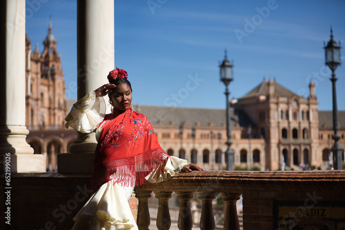 Young black and South American woman in a beige gypsy flamenco suit, posing in a beautiful square in the city of Seville in Spain. Concept dance, folklore, flamenco, art.