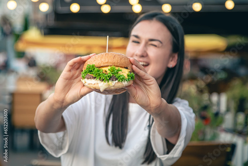 A young woman eating burger in street cafe.