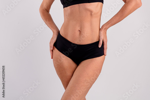 Closeup healthy fit slim body belly sportive elderly woman demonstrate black cotton lingerie posing isolated over gray color background