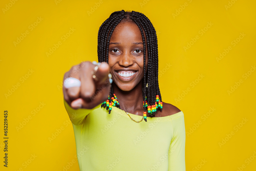 Young african woman points finger directly at camera with positive expression, says I choose you, wears casual outfit and braid hair, stands over yellow wall with blank space area. You are my type. - obrazy, fototapety, plakaty 