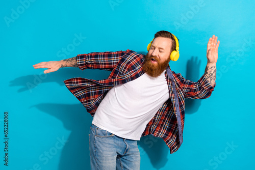 Portrait of crazy funky man with tattoo wear plaid shirt dancing in headphones listen upbeat music isolated on blue color background