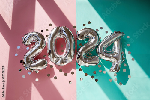 Silver numbers 2024 new year balloons among confetti in sunlight on pink turquoise background Happy new year celebration party. Greetings and congratulation photo
