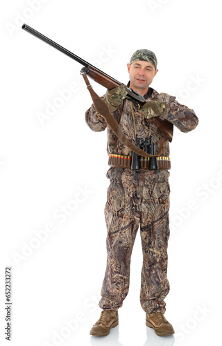 Full length portrait of duck hunter with a rifle and binoculars aiming a gun isolated on white background. Fifty-year-old man in hunting uniform shoots with a rifle to the side and posing in studio.