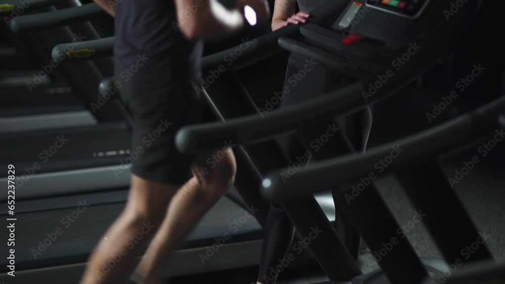 Night training, anonymous man runner run on a treadmill, aerobic exercise and endurance training in the gym with female coach, view of the legs. Night training, anonymous man runner run on a treadmill, aerobic exercise and endurance training in the gym with female coach, view of the legs.