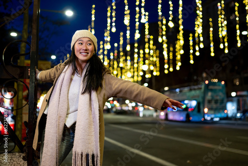 Happy young lady enjoying christmas lights in the street. Beautiful woman having fun at night in the city during winter.