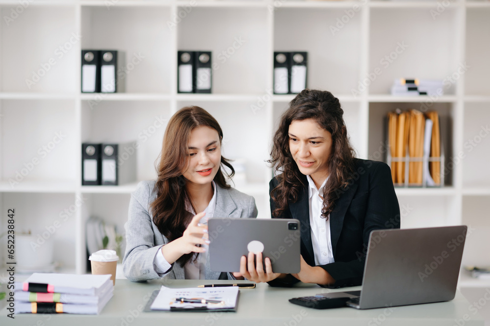 Two businesswoman discuss investment project working and planning strategy with tablet laptop computer in office.. Two businesswoman discuss investment project working and planning strategy with tablet laptop computer in office..