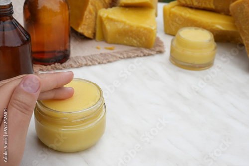 Woman hands using beeswax ointment. Medicinal cream from beeswax good for skin. Ingredients for making homemade skin cream on background. Side view.