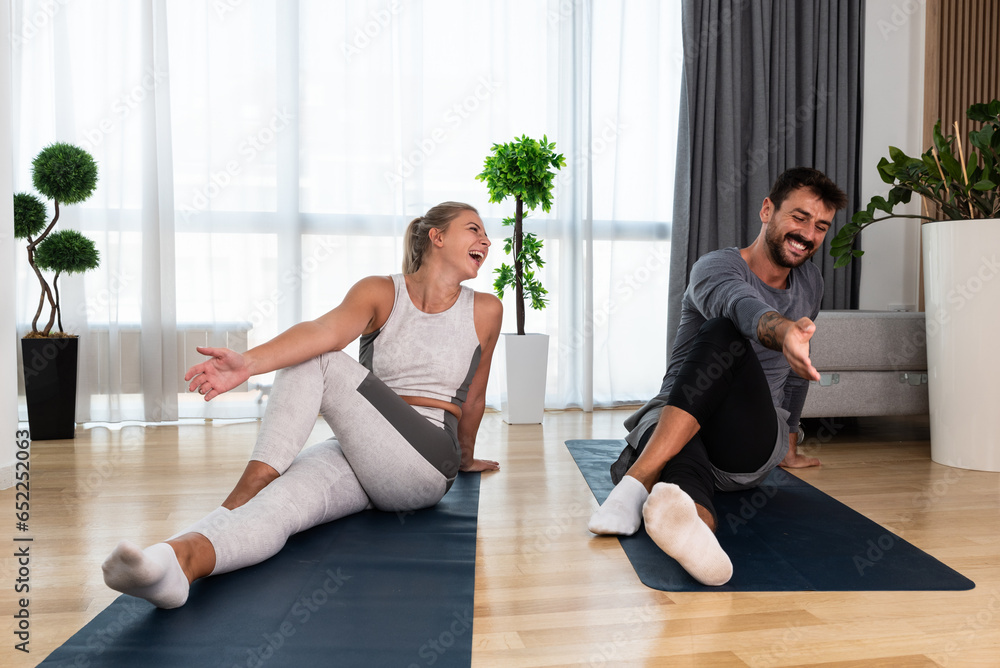Couple exercising together. Man and woman in sportswear doing workout at home. Partners doing yoga class in the apartment on yoga mats stretching muscles breathing exercises after stress at work Couple exercising together. Man and woman in sportswear doing workout at home. Partners doing yoga class in the apartment on yoga mats stretching muscles breathing exercises after stress at work